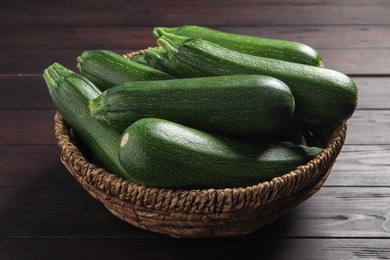 Photo of Raw ripe zucchinis in wicker bowl on wooden table