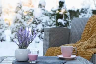 Photo of Candle, potted flowers and cup of hot drink on coffee table outdoors. Cosy winter