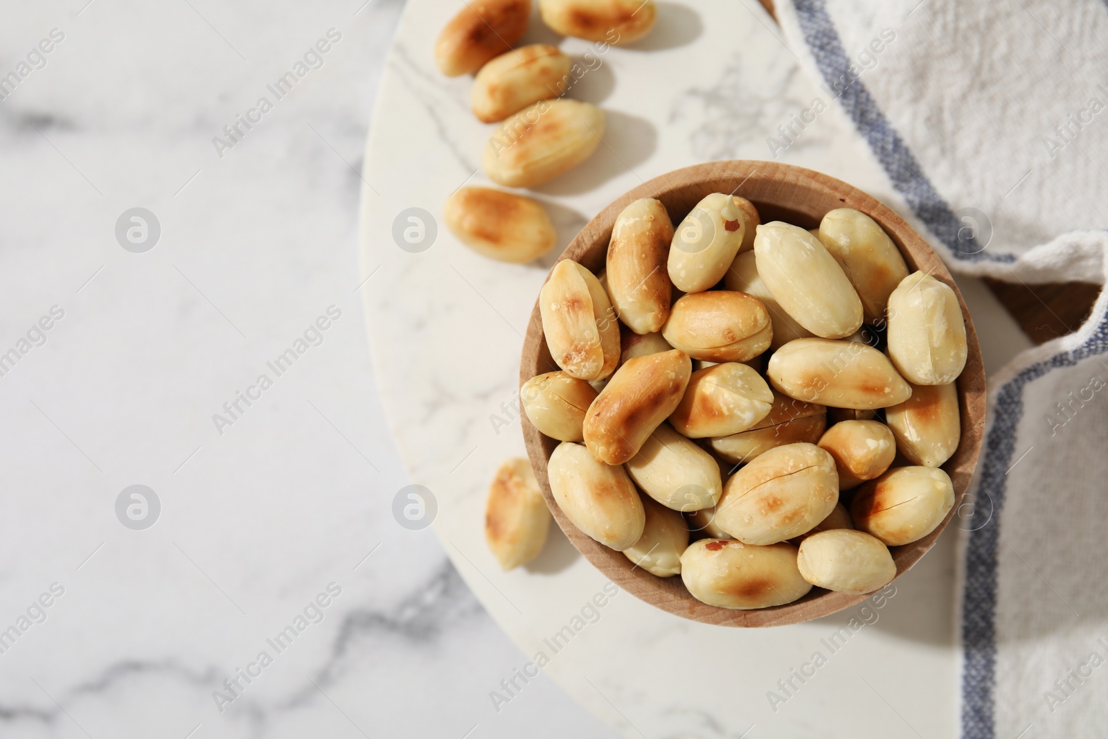 Photo of Roasted peanuts in bowl on white marble table, top view. Space for text