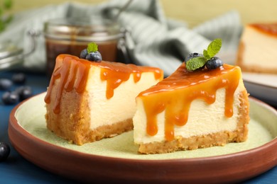 Photo of Pieces of delicious caramel cheesecake with blueberry and mint on blue table, closeup