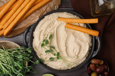Photo of Delicious hummus with grissini sticks served on grey table, flat lay