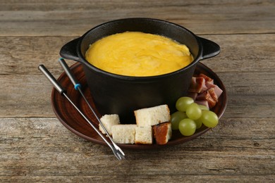 Fondue pot with melted cheese and different products on wooden table