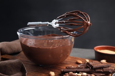 Bowl of chocolate cream, whisk and ingredients on table, closeup