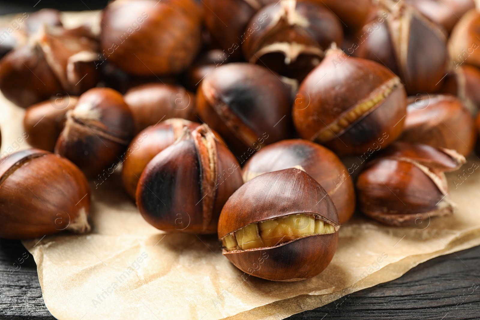 Photo of Tasty roasted edible chestnuts on black wooden table, closeup