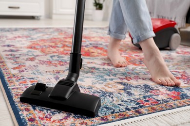 Woman cleaning carpet with vacuum cleaner at home, closeup