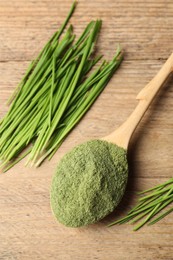 Wheat grass powder in spoon and fresh green sprouts on wooden table, flat lay