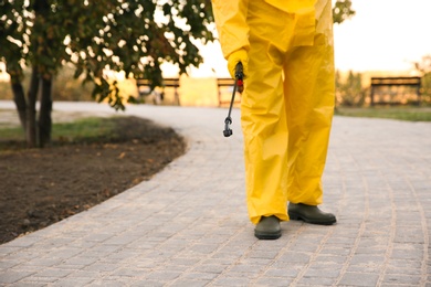 Photo of Person in hazmat suit disinfecting pavement in park with sprayer, closeup. Surface treatment during coronavirus pandemic