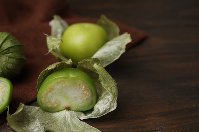Photo of Fresh green tomatillos with husk on wooden table, closeup. Space for text