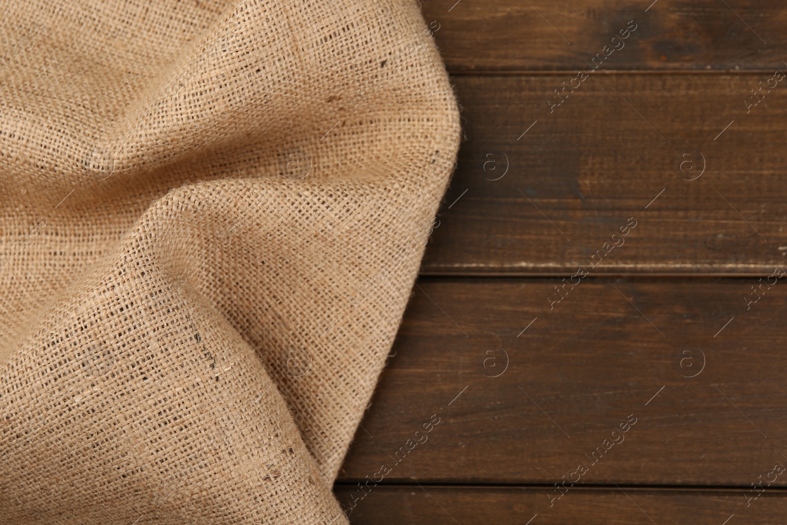 Photo of Brown burlap fabric on wooden table, top view. Space for text