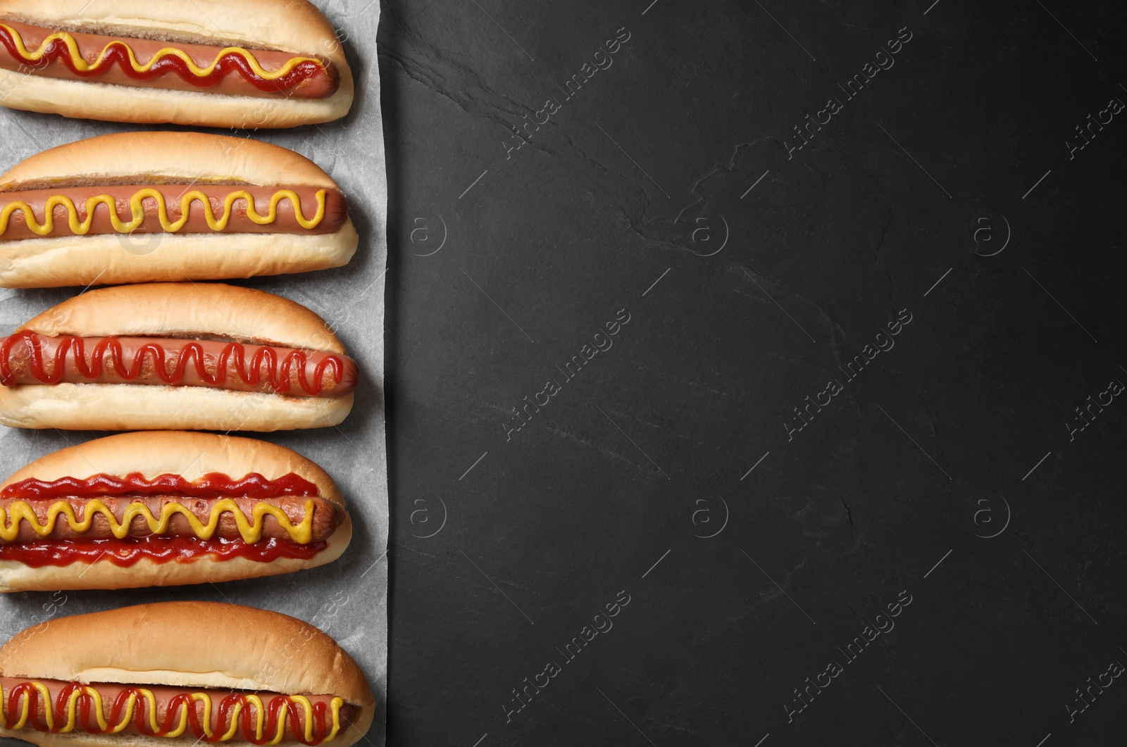 Photo of Fresh delicious hot dogs with sauces on black table, top view. Space for text