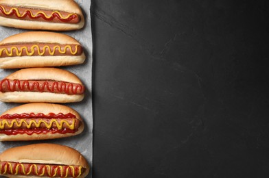 Photo of Fresh delicious hot dogs with sauces on black table, top view. Space for text