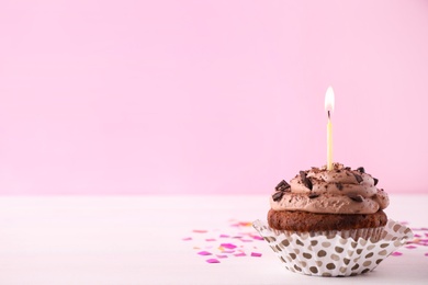 Photo of Chocolate cupcake with burning candle on white table against pink background. Space for text
