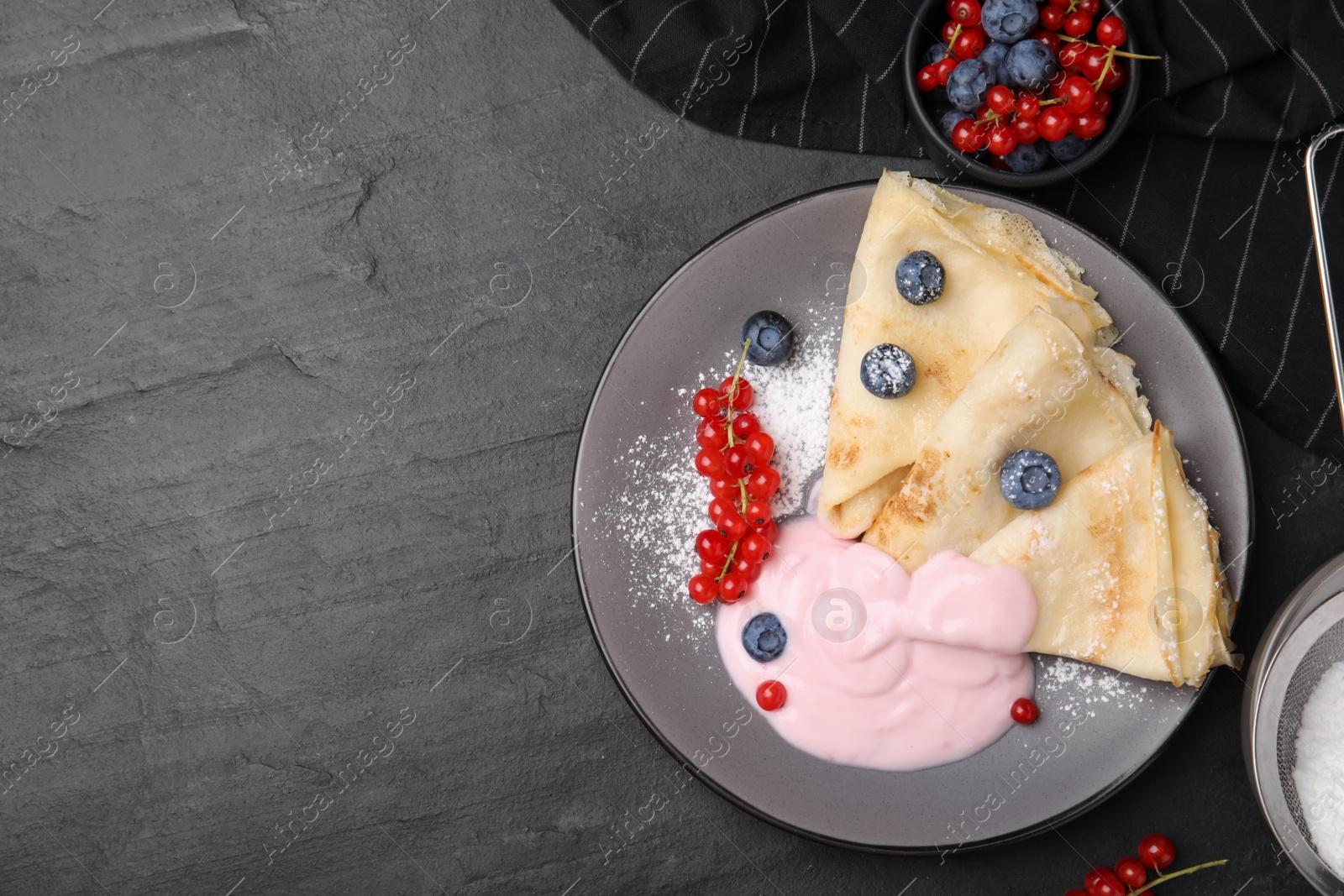 Photo of Delicious crepes with natural yogurt, blueberries and red currants on dark grey table, flat lay. Space for text