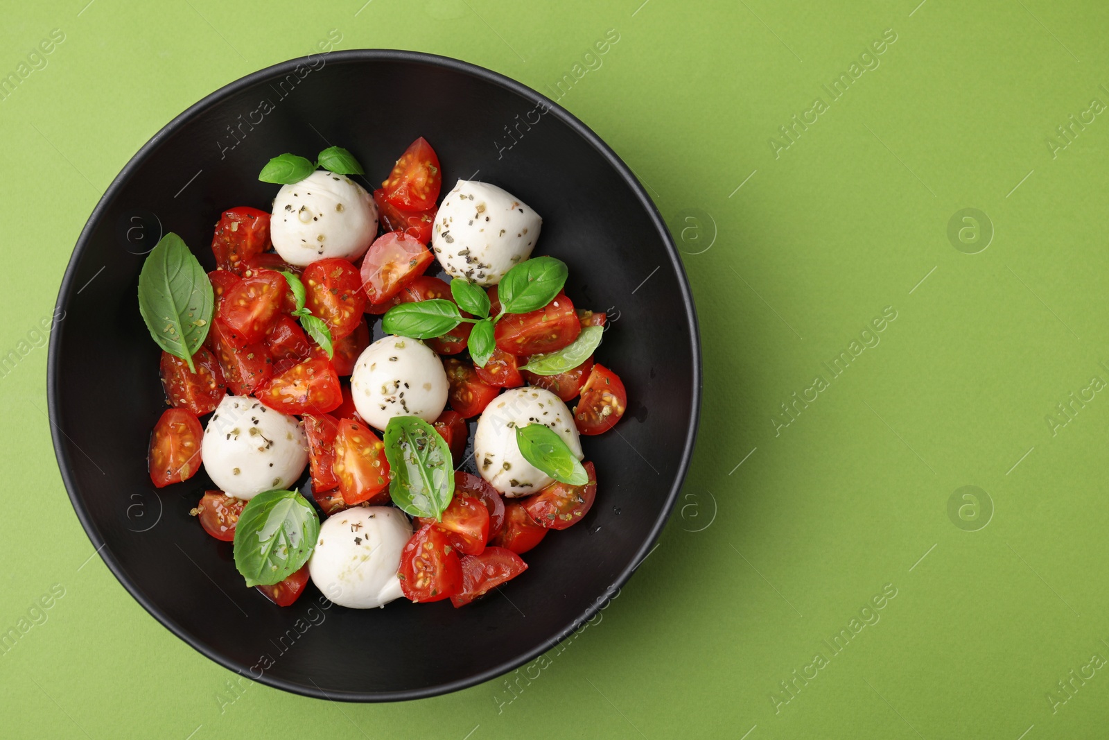 Photo of Tasty salad Caprese with tomatoes, mozzarella balls and basil on green background, top view. Space for text