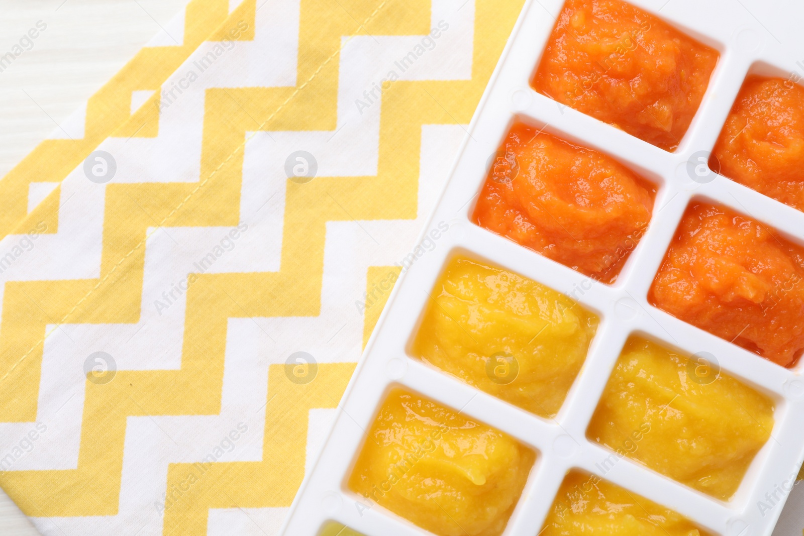 Photo of Different purees in ice cube tray ready for freezing on table, top view. Space for text