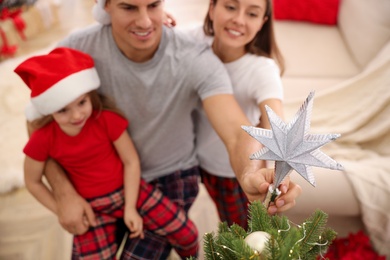 Photo of Family decorating Christmas tree indoors, focus on star topper
