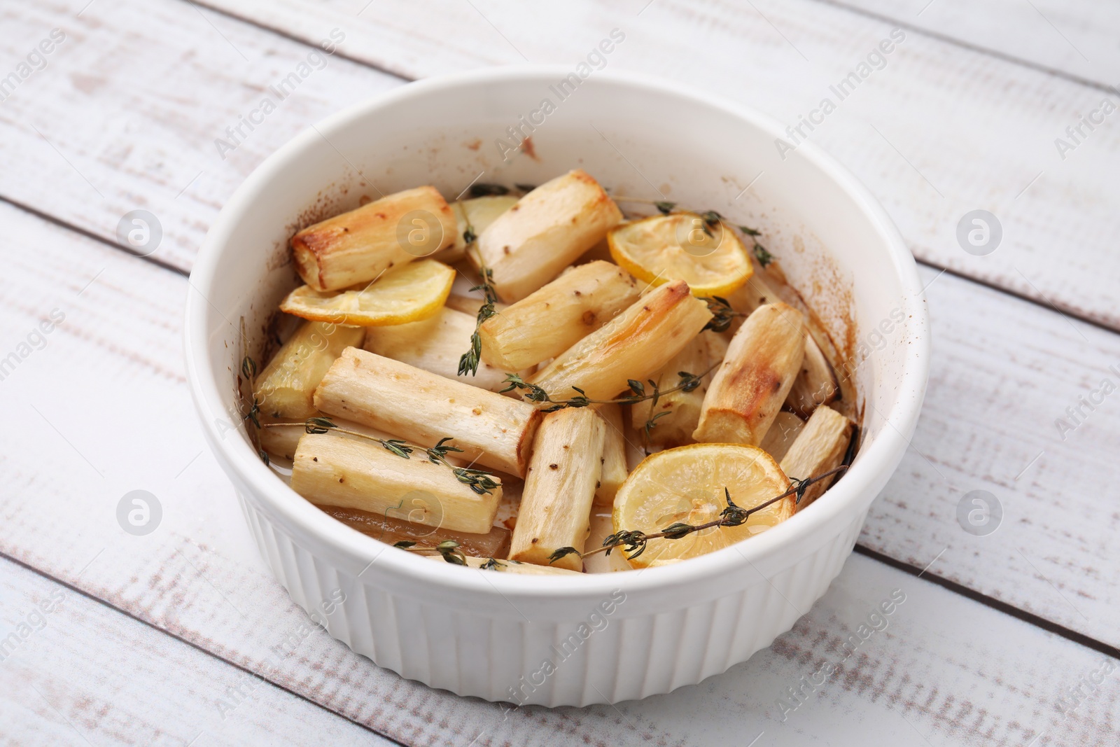 Photo of Dish with baked salsify roots, lemon and thyme on white wooden table, closeup