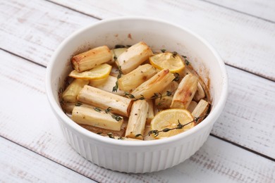 Photo of Dish with baked salsify roots, lemon and thyme on white wooden table, closeup