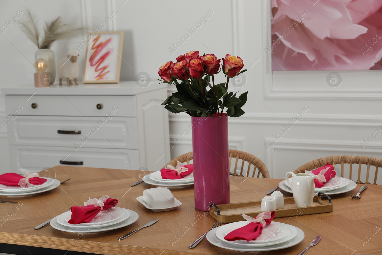 Photo of Color accent table setting. Plates, cutlery, pink napkins and vase with beautiful roses in dining room