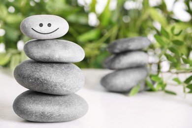 Stack of stones with drawn happy face on white table, space for text. Be in harmony and enjoying your life