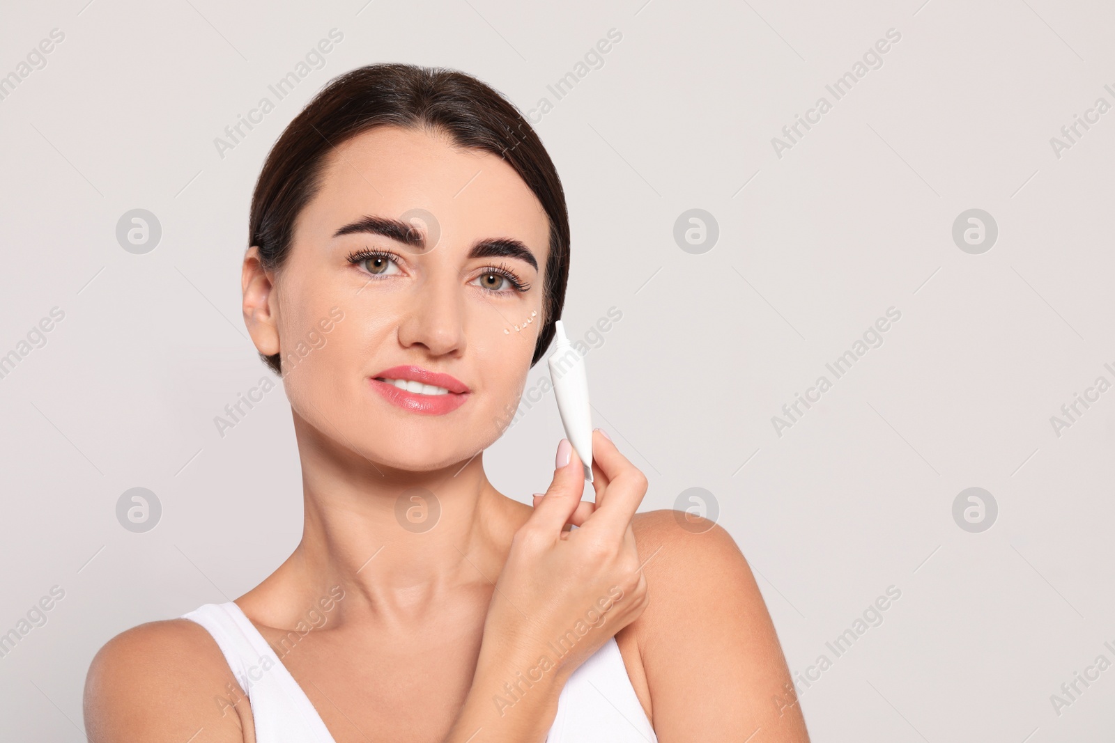 Photo of Woman with cosmetic product around eye on light background. Space for text