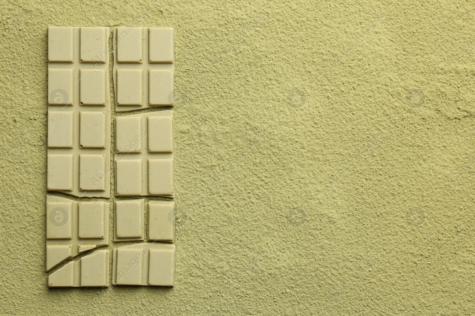 Photo of Pieces of tasty matcha chocolate bar on green powder, top view. Space for text