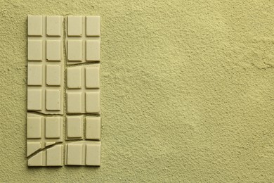 Pieces of tasty matcha chocolate bar on green powder, top view. Space for text