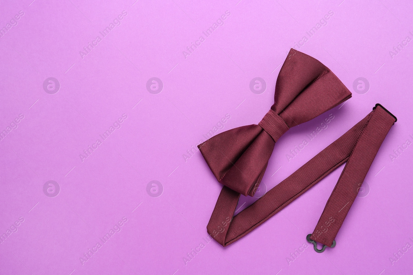 Photo of Stylish burgundy bow tie on violet background, top view. Space for text