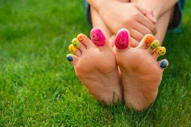 Photo of Teenage girl with smiling faces drawn on toes outdoors, closeup