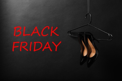 Photo of Hanger with pair of elegant shoes and words Black Friday on dark background