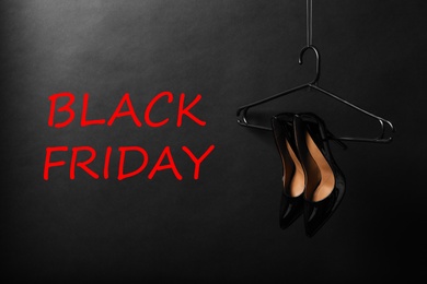 Hanger with pair of elegant shoes and words Black Friday on dark background