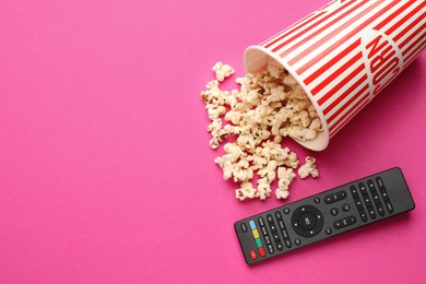 Photo of Remote control and cup of popcorn on pink background, flat lay. Space for text