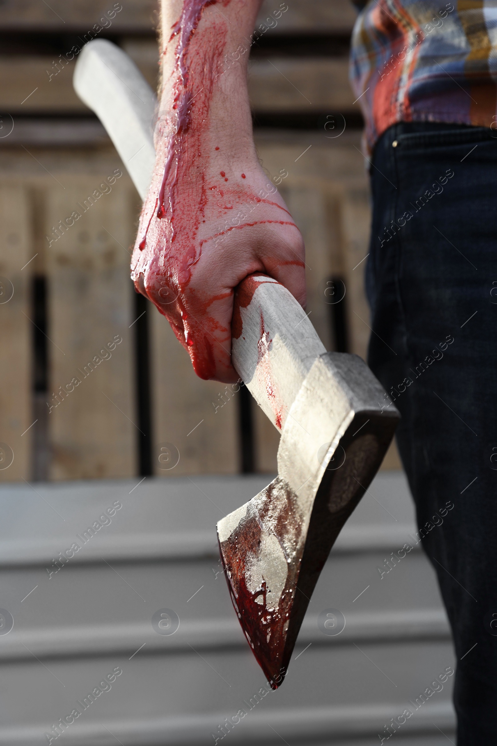 Photo of Man holding bloody axe outdoors, closeup view