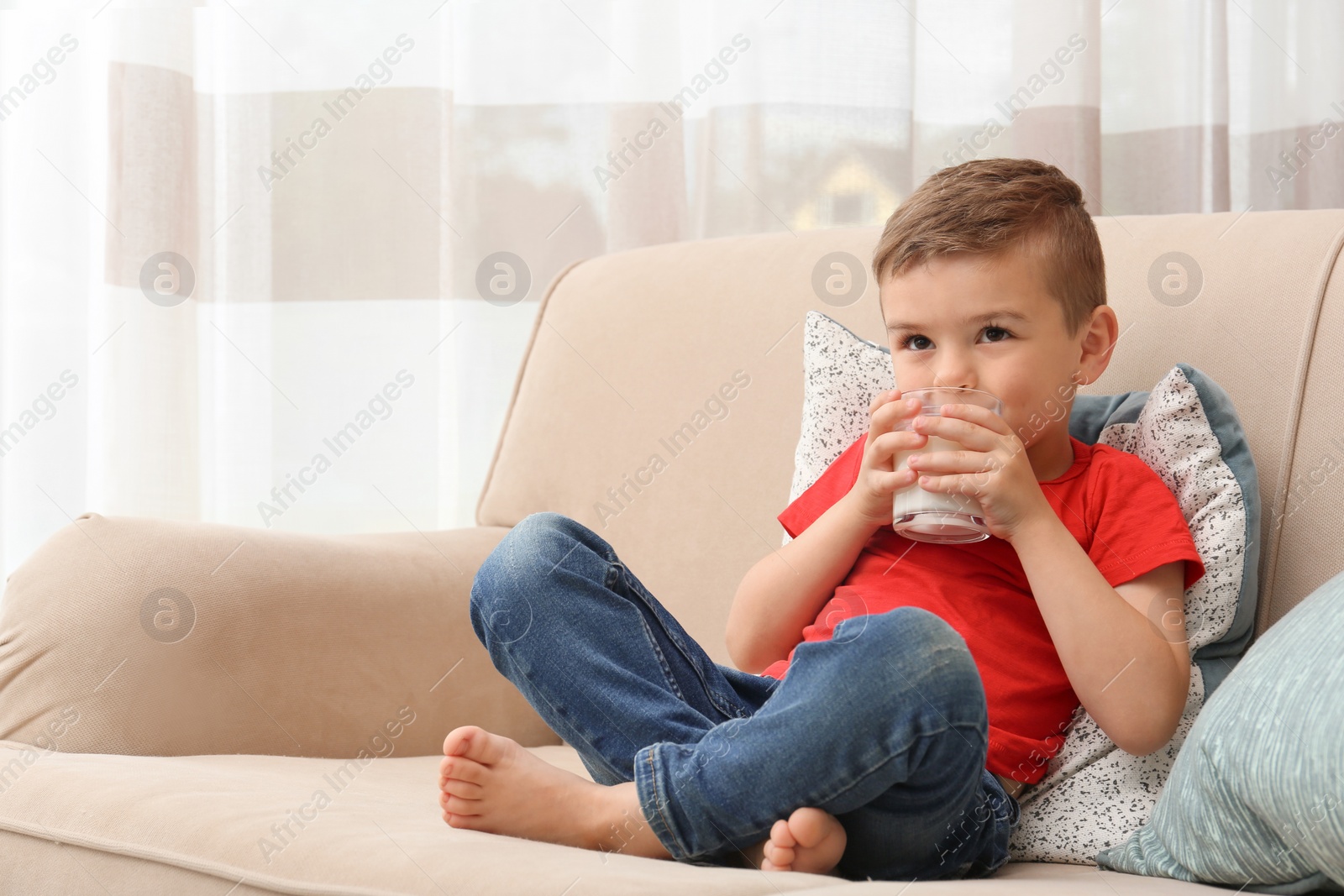 Photo of Cute little boy drinking milk on sofa at home