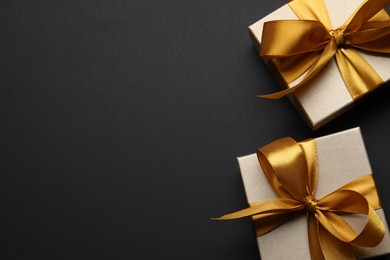 Photo of Golden gift boxes on black background, flat lay. Space for text