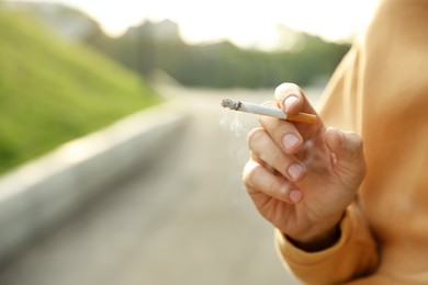 Photo of Man with cigarette outdoors, closeup of hand. Space for text