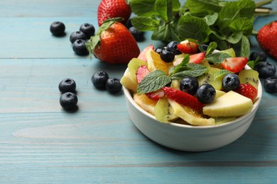 Photo of Tasty fruit salad in bowl and ingredients on light blue wooden table, closeup