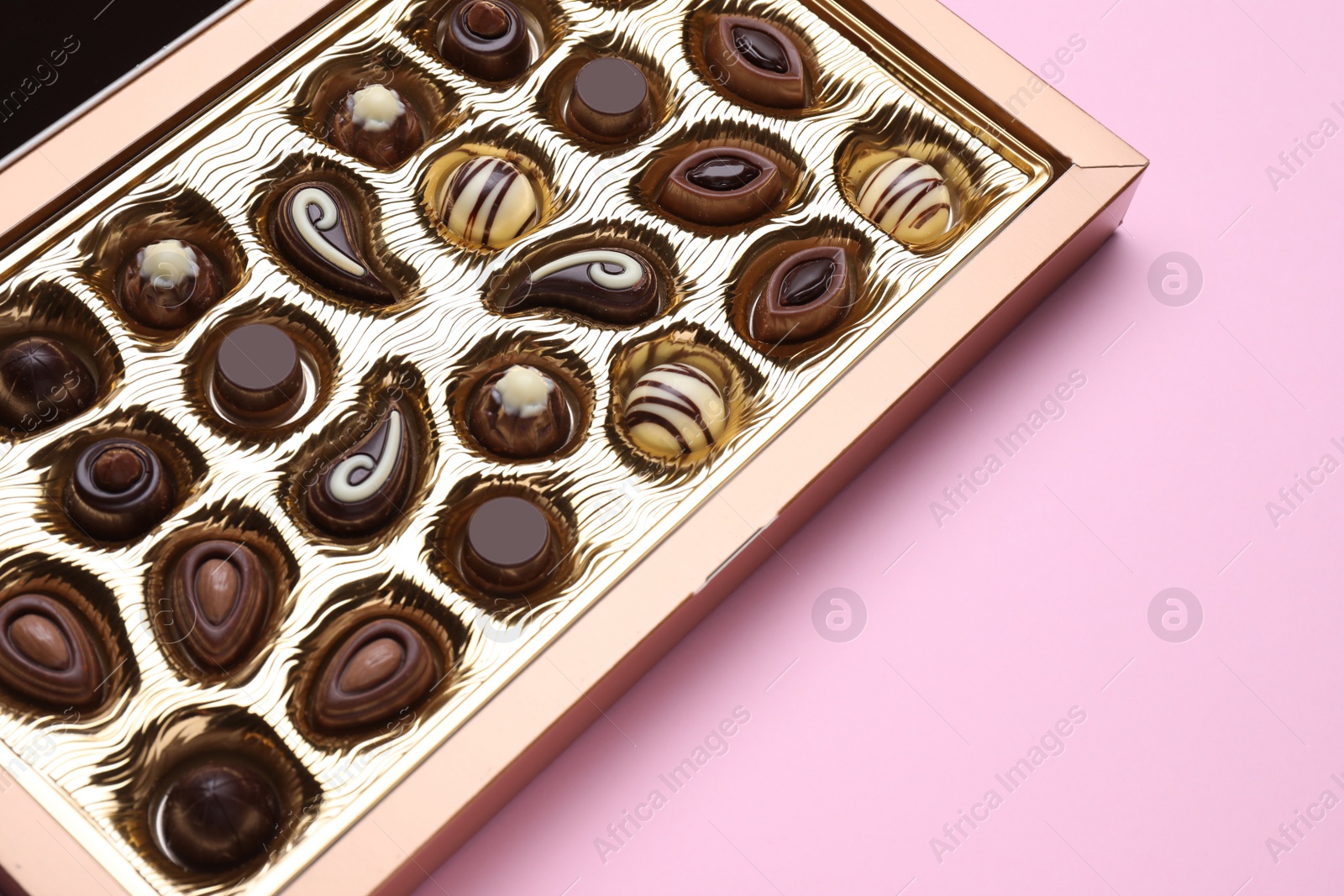 Photo of Box of delicious chocolate candies on pink background, closeup