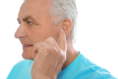 Mature man adjusting hearing aid on white background