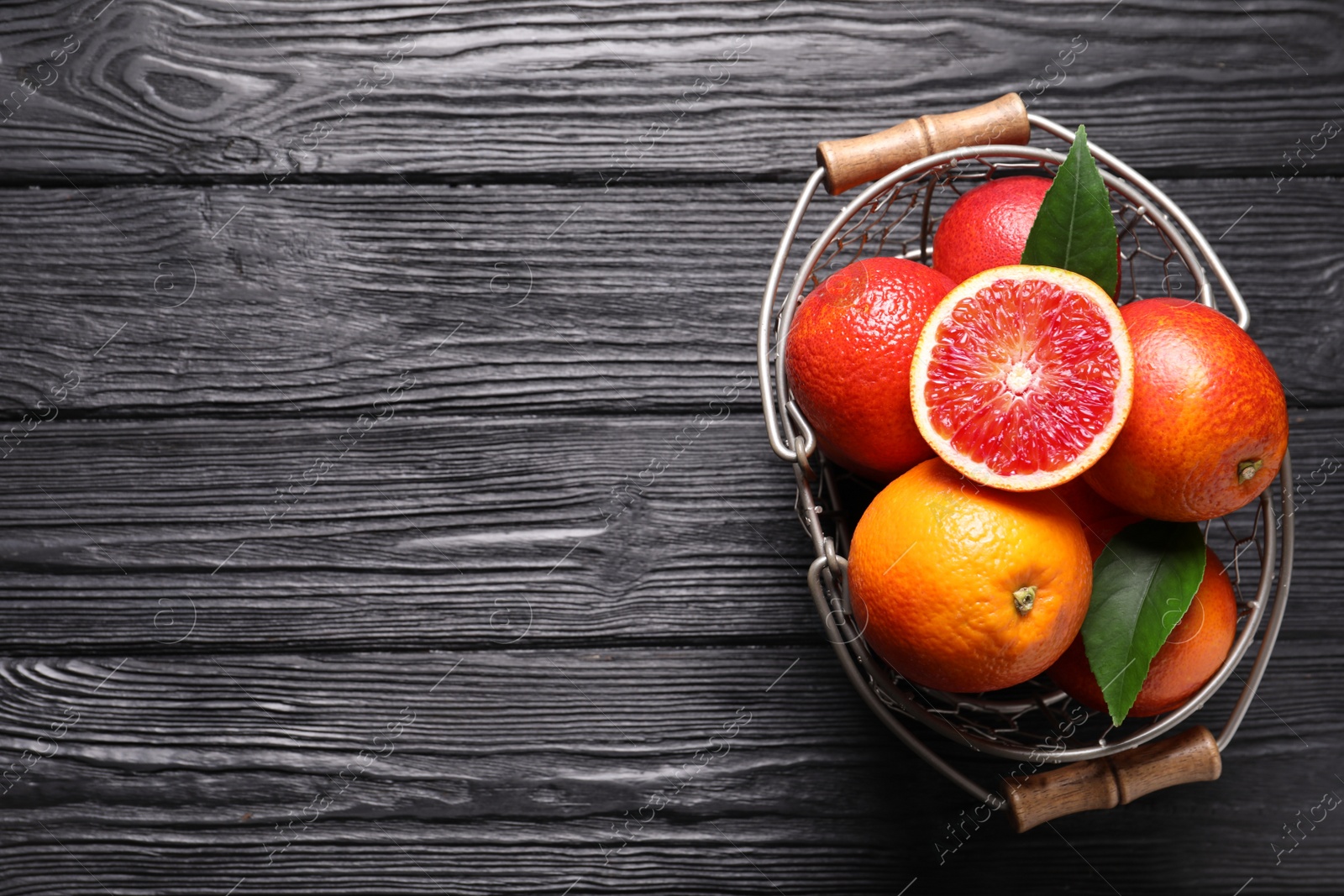 Photo of Whole and cut red oranges on black wooden table, top view. Space for text