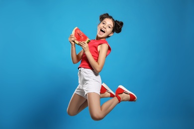 Photo of Cute little girl with watermelon jumping on blue background