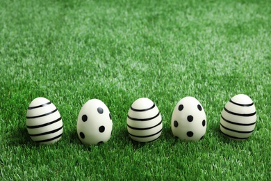 Photo of Line of traditional Easter eggs decorated with black paint on green lawn, space for text