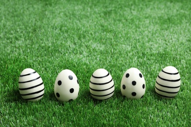 Line of traditional Easter eggs decorated with black paint on green lawn, space for text