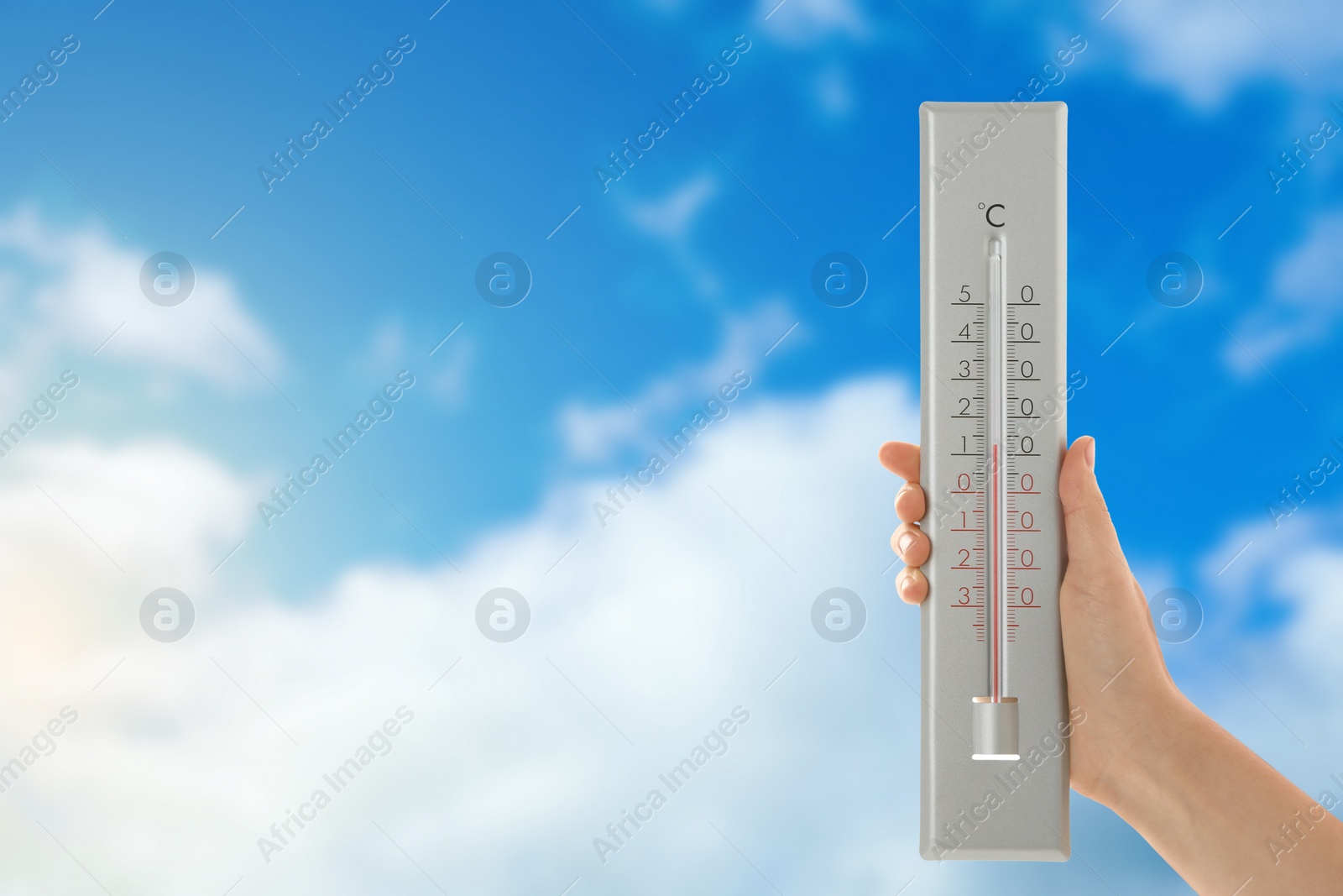 Image of Woman holding thermometer against blue sky, closeup. Space for text