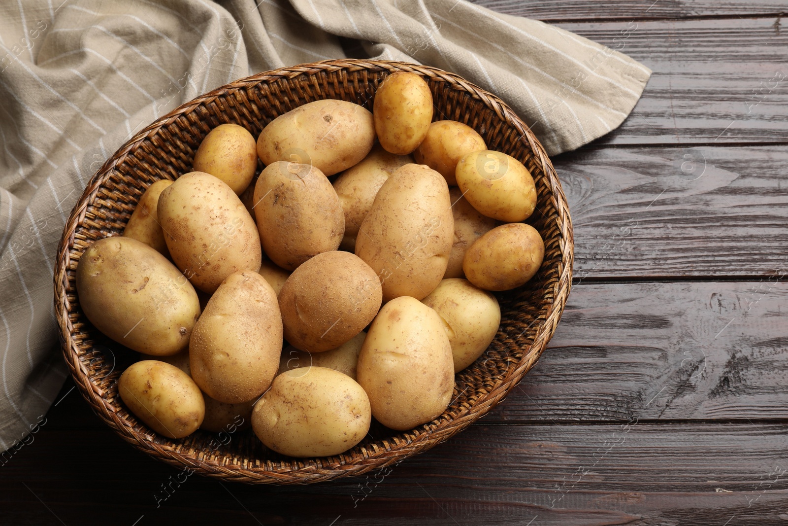 Photo of Raw fresh potatoes in wicker basket on wooden table, top view. Space for text