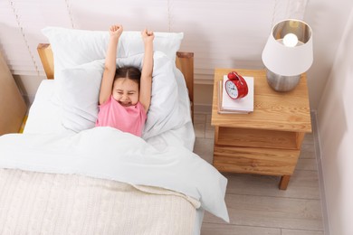 Photo of Cute little girl stretching in cosy bedroom, above view