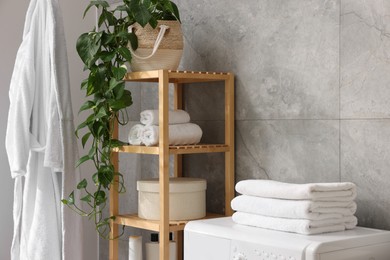 Photo of Soft towels, houseplant, box and shelving unit indoors