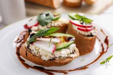 Photo of Delicious bruschettas with cream cheese, vegetables and balsamic vinegar on white plate, closeup