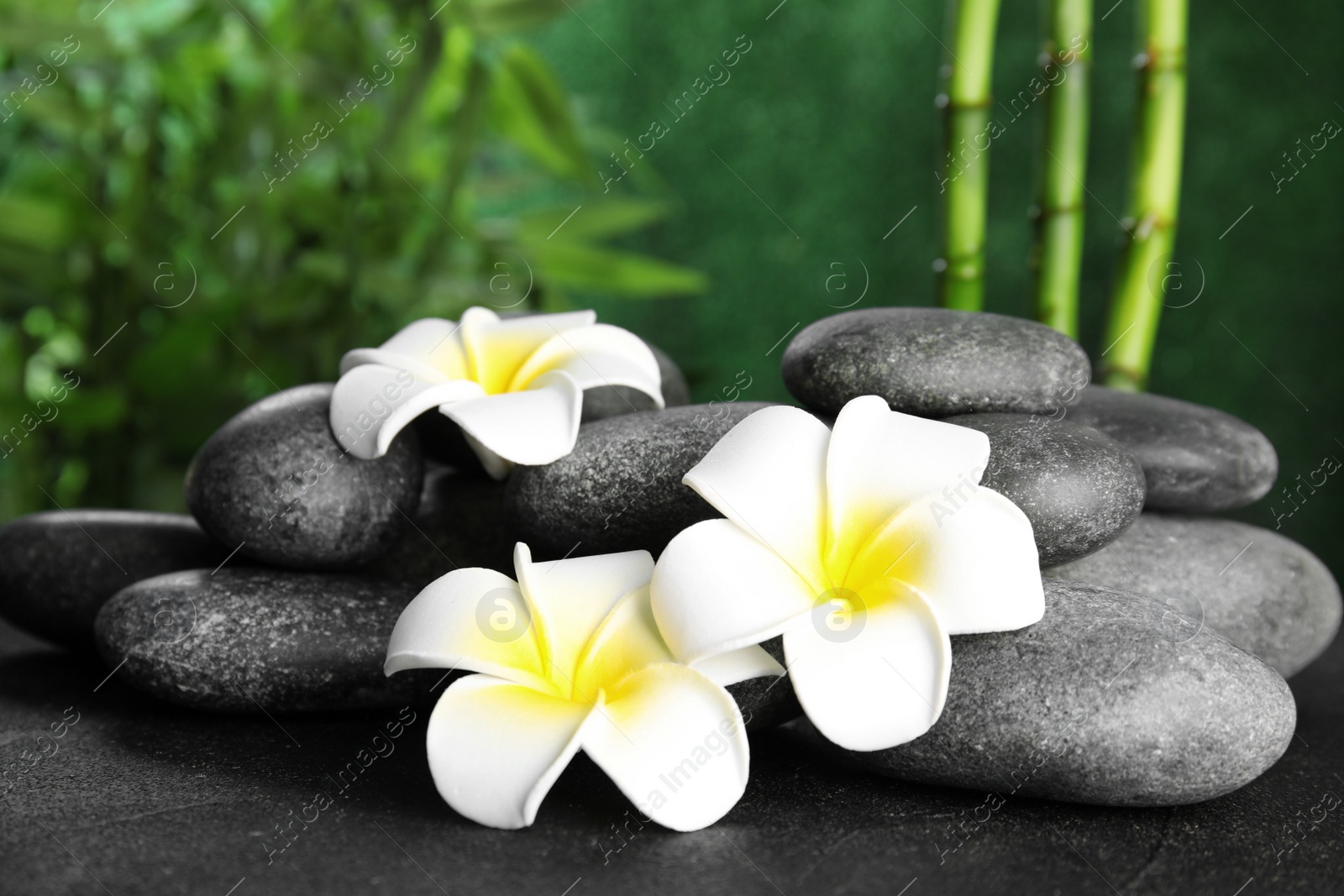 Photo of Zen stones and exotic flowers on table against blurred background