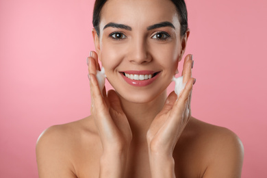 Photo of Young woman applying cosmetic product on pink background, closeup. Washing routine